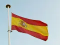 Spanska flaggan vajar i vinden. Den har tre horisontella band: rött, gult och rött. I det gula bandet finns Spaniens riksvapen. Orden "spanska ord" kan associeras med denna flagga.