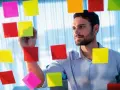 Man med skägg fäster post-it-lappar på en glasvägg, som en del av processen att skriva debattartikel.