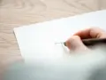 En hand skriver ord på ett papper, kanske en dikt om sorg och saknad.