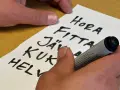 En hand skriver en svordomar lista på ett papper. Orden "hora", "fitta", "jäv", "kuk" och "helv" syns tydligt.