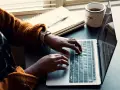 Person skriver på en laptop, med en anteckningsbok och kaffemugg bredvid. Kanske en guide om hur man skriver en novell.