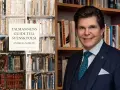 Andreas Norlén presenterar "Talmannens guide till svensk poesi", en samling bra dikter. Bakom honom syns bokhyllor fyllda med litteratur.