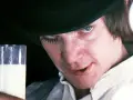 En ung man med hatt och falska ögonfransar håller ett glas mjölk. Vem skrev A Clockwork Orange? Anthony Burgess.