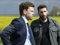 Två män står i en gul rapsåker. Den ena bär kostym, den andra en militärjacka. Scen från avdelning q film.