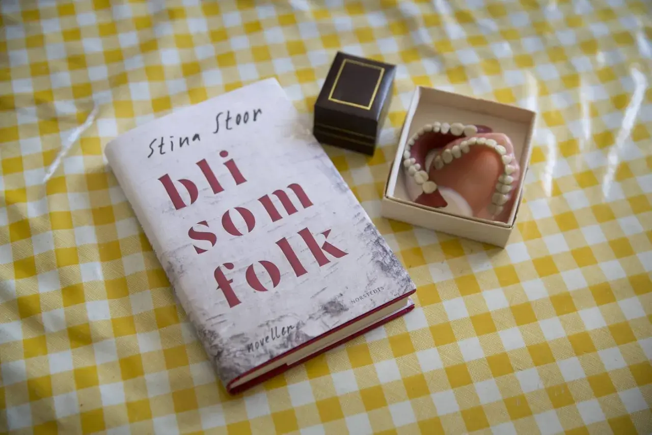 Boken "Bli som folk" av Stina Stoor ligger på ett gult rutigt bord bredvid ett par proteser.