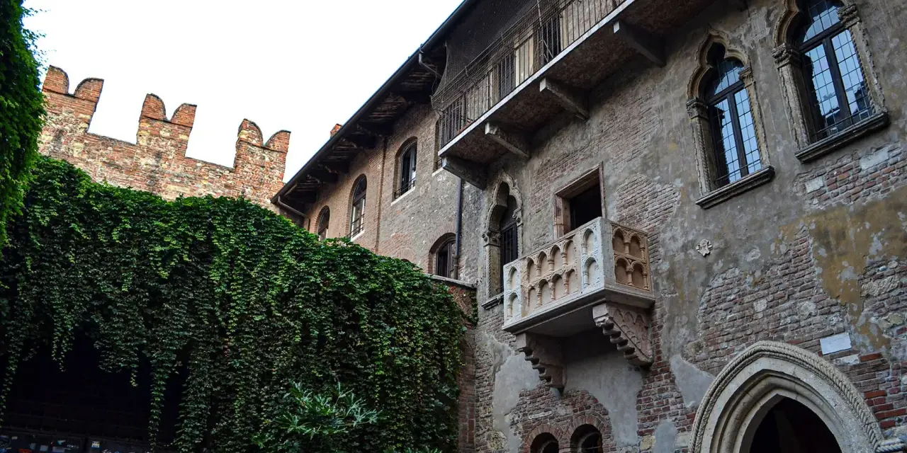 A historic brick building with ivy-covered walls and Juliet's balcony in Verona, Italy.