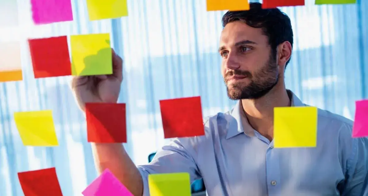 Man med skägg fäster post-it-lappar på en glasvägg, som en del av processen att skriva debattartikel.