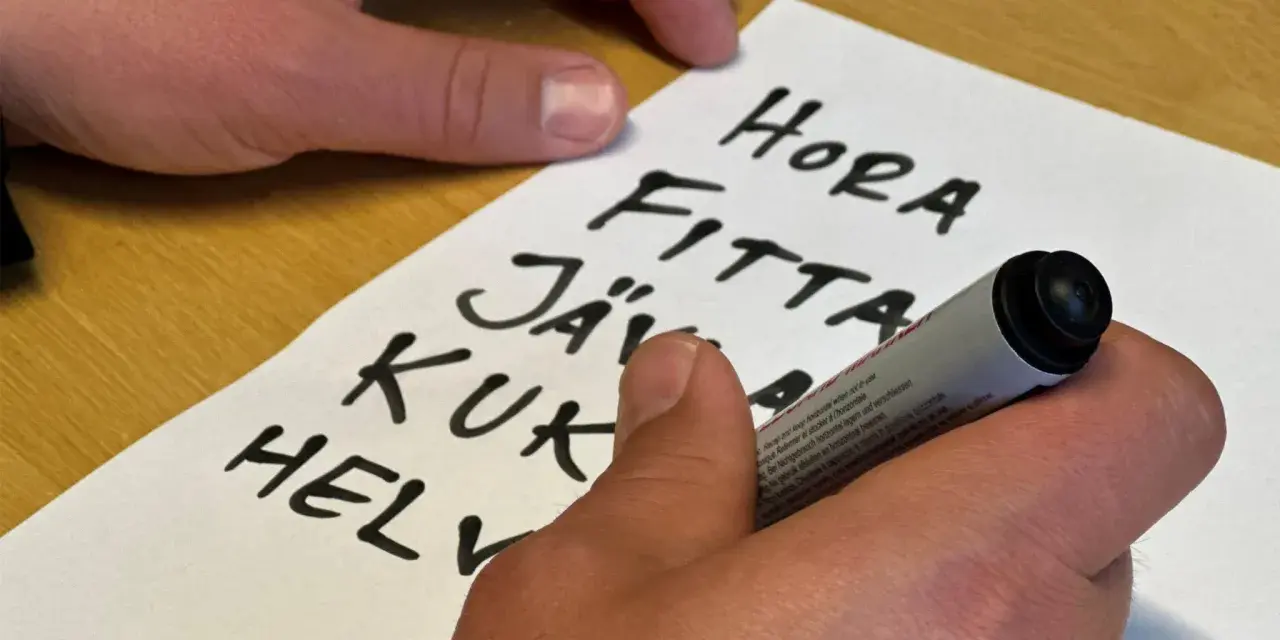 En hand skriver en svordomar lista på ett papper. Orden "hora", "fitta", "jäv", "kuk" och "helv" syns tydligt.
