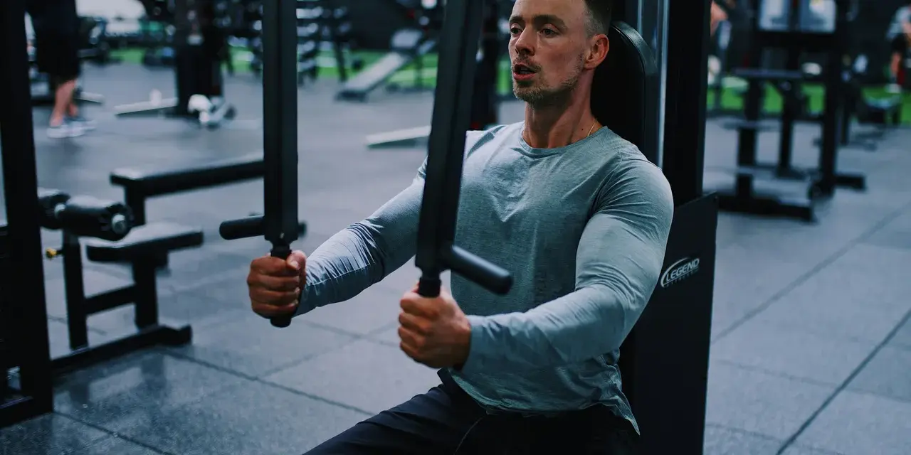 Man tränar bröstmusklerna på ett gym. Han använder en maskin för att hårddra sina muskler och bygga styrka.