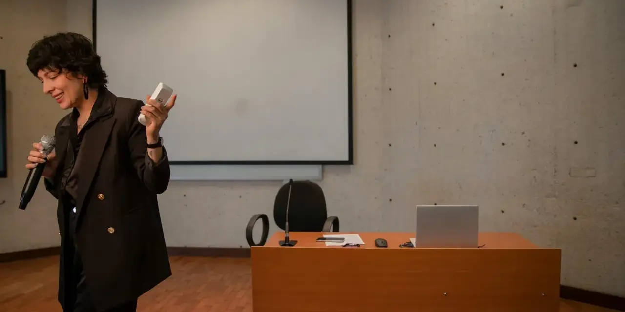 En kvinna håller mikrofon och en fjärrkontroll, redo att presentera en tes.