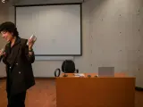 En kvinna håller mikrofon och en fjärrkontroll, redo att presentera en tes.