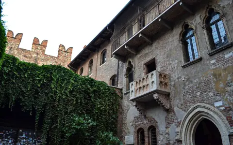A historic brick building with ivy-covered walls and Juliet's balcony in Verona, Italy.