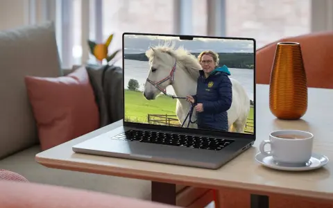 En kvinna med glasögon och en blå jacka håller i en vit häst på en laptop. Bilden visar vad referat betyder: en sammanfattning av en händelse.