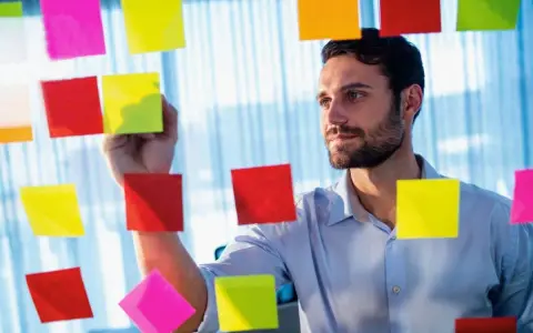 Man med skägg fäster post-it-lappar på en glasvägg, som en del av processen att skriva debattartikel.