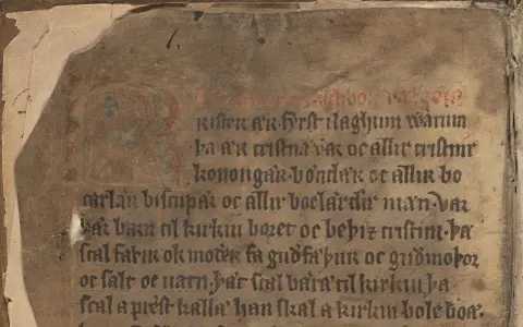 Gammal handskrift med text i mörka bokstäver och röd initial. Texten är skriven i ett medeltida versmått.