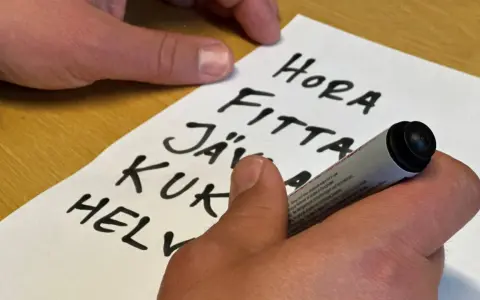 En hand skriver en svordomar lista på ett papper. Orden "hora", "fitta", "jäv", "kuk" och "helv" syns tydligt.