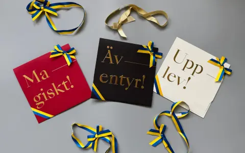 Grattis! Kort med texten "Magiskt!", "Äventyr!" och "Upplev!" i guldfärgad skrivstil, dekorerade med blågula band.