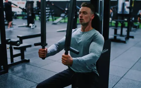 Man tränar bröstmusklerna på ett gym. Han använder en maskin för att hårddra sina muskler och bygga styrka.