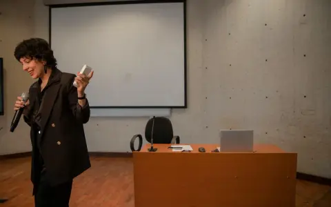 En kvinna håller mikrofon och en fjärrkontroll, redo att presentera en tes.