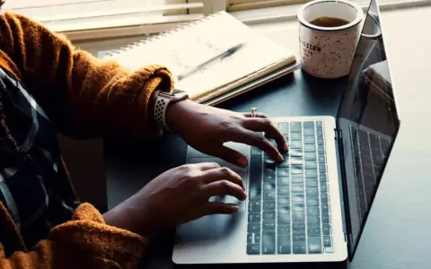 Person skriver på en laptop, med en anteckningsbok och kaffemugg bredvid. Kanske en guide om hur man skriver en novell.