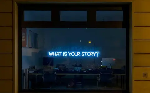 Blå neontext "WHAT IS YOUR STORY?" lyser i ett fönster, som en inbjudan till en skrivarkurs online.