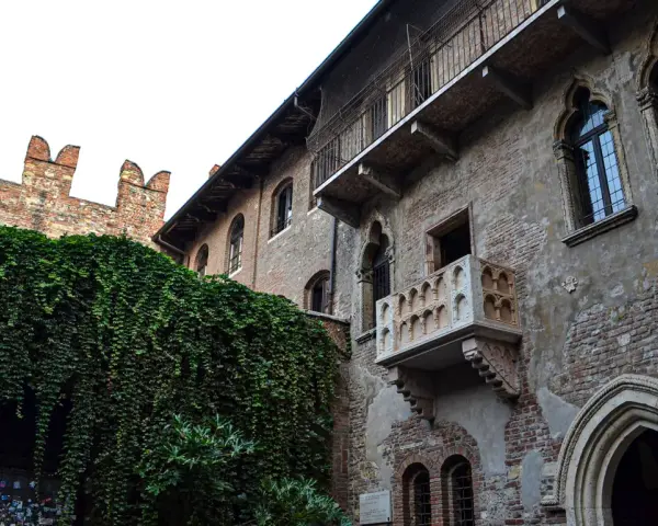 A historic brick building with ivy-covered walls and Juliet's balcony in Verona, Italy.