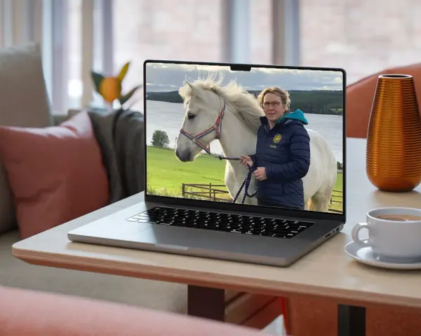 En kvinna med glasögon och en blå jacka håller i en vit häst på en laptop. Bilden visar vad referat betyder: en sammanfattning av en händelse.
