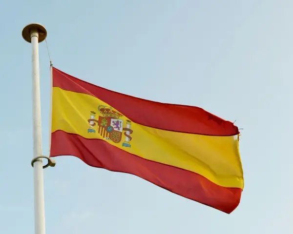 Spanska flaggan vajar i vinden. Den har tre horisontella band: rött, gult och rött. I det gula bandet finns Spaniens riksvapen. Orden "spanska ord" kan associeras med denna flagga.