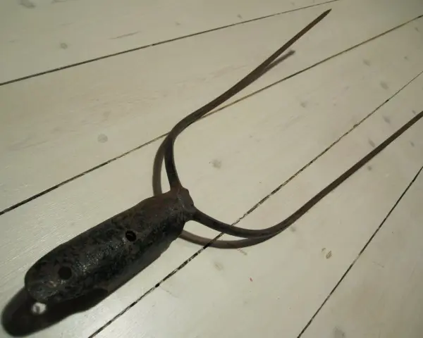 A rusty, old pitchfork with three tines lies on a white wooden floor.