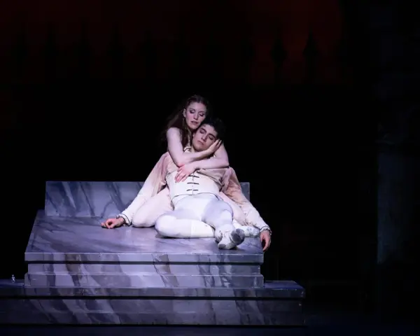 En kvinna med rött hår omfamnar en sovande man på en marmorplattform. En scen som påminner om vem skrev Romeo och Julia.