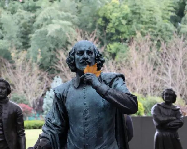 Staty av Shakespeare med ett löv framför munnen, som ett sonett exempel. Bakom syns andra statyer och träd.