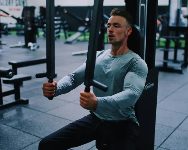 Man tränar bröstmusklerna på ett gym. Han använder en maskin för att hårddra sina muskler och bygga styrka.