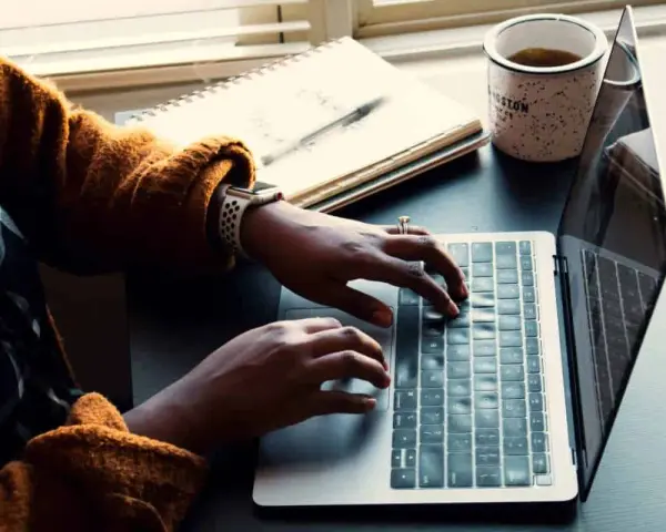 Person skriver på en laptop, med en anteckningsbok och kaffemugg bredvid. Kanske en guide om hur man skriver en novell.