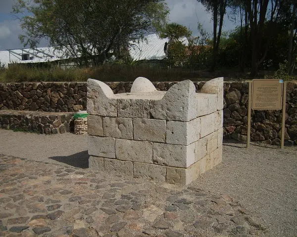 Stenbyggnad, en sorts altare synonym, står på en stenlagd yta. Bakom syns en mur av stenar och träd.