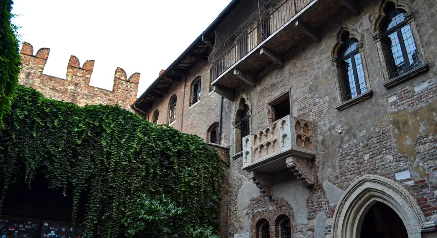 A historic brick building with ivy-covered walls and Juliet's balcony in Verona, Italy.