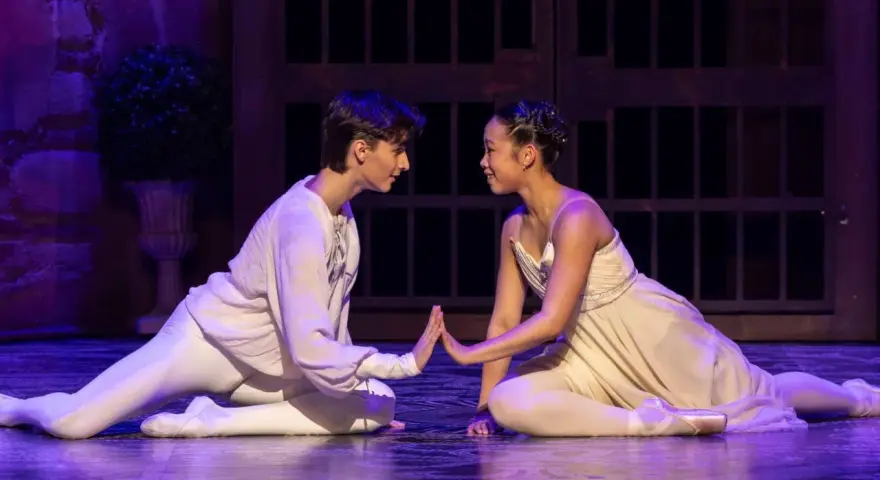 Romeo och Julia handling: Två dansare i balettkläder, en man i vitt och en kvinna i ljusgult, möts på scenen med händerna mot varandra.