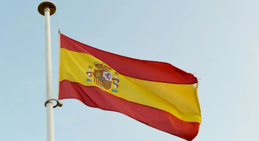 Spanska flaggan vajar i vinden. Den har tre horisontella band: rött, gult och rött. I det gula bandet finns Spaniens riksvapen. Orden "spanska ord" kan associeras med denna flagga.