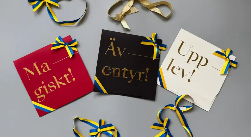 Grattis! Kort med texten "Magiskt!", "Äventyr!" och "Upplev!" i guldfärgad skrivstil, dekorerade med blågula band.