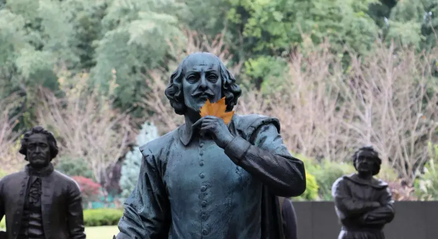 Staty av Shakespeare med ett löv framför munnen, som ett sonett exempel. Bakom syns andra statyer och träd.