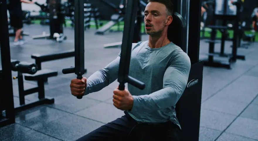 Man tränar bröstmusklerna på ett gym. Han använder en maskin för att hårddra sina muskler och bygga styrka.
