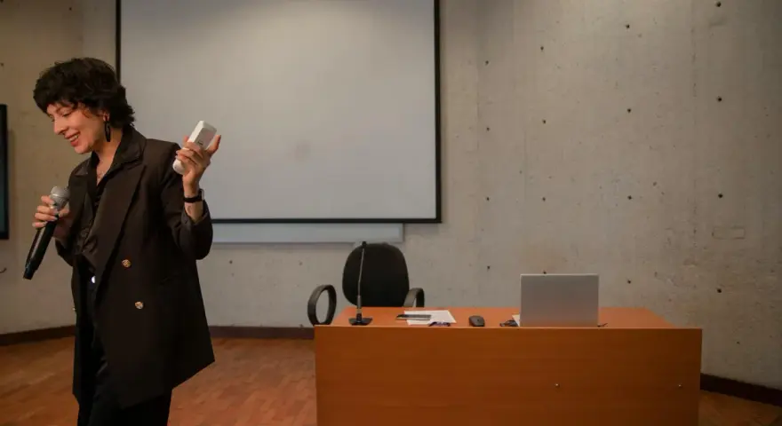 En kvinna håller mikrofon och en fjärrkontroll, redo att presentera en tes.