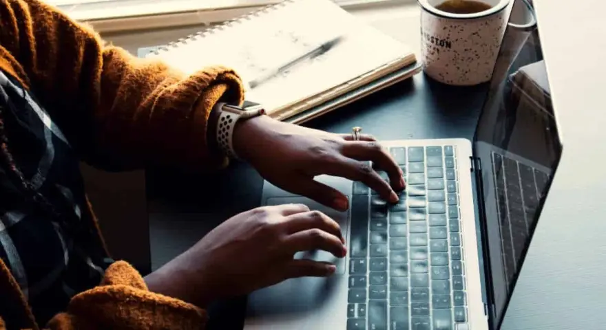 Person skriver på en laptop, med en anteckningsbok och kaffemugg bredvid. Kanske en guide om hur man skriver en novell.