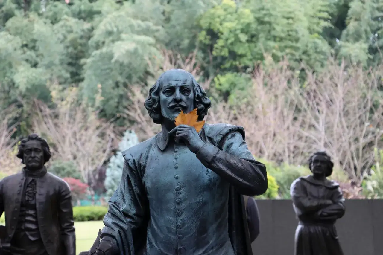 Staty av Shakespeare med ett l&ouml;v framf&ouml;r munnen, som ett sonett exempel. Bakom syns fler statyer och tr&auml;d.