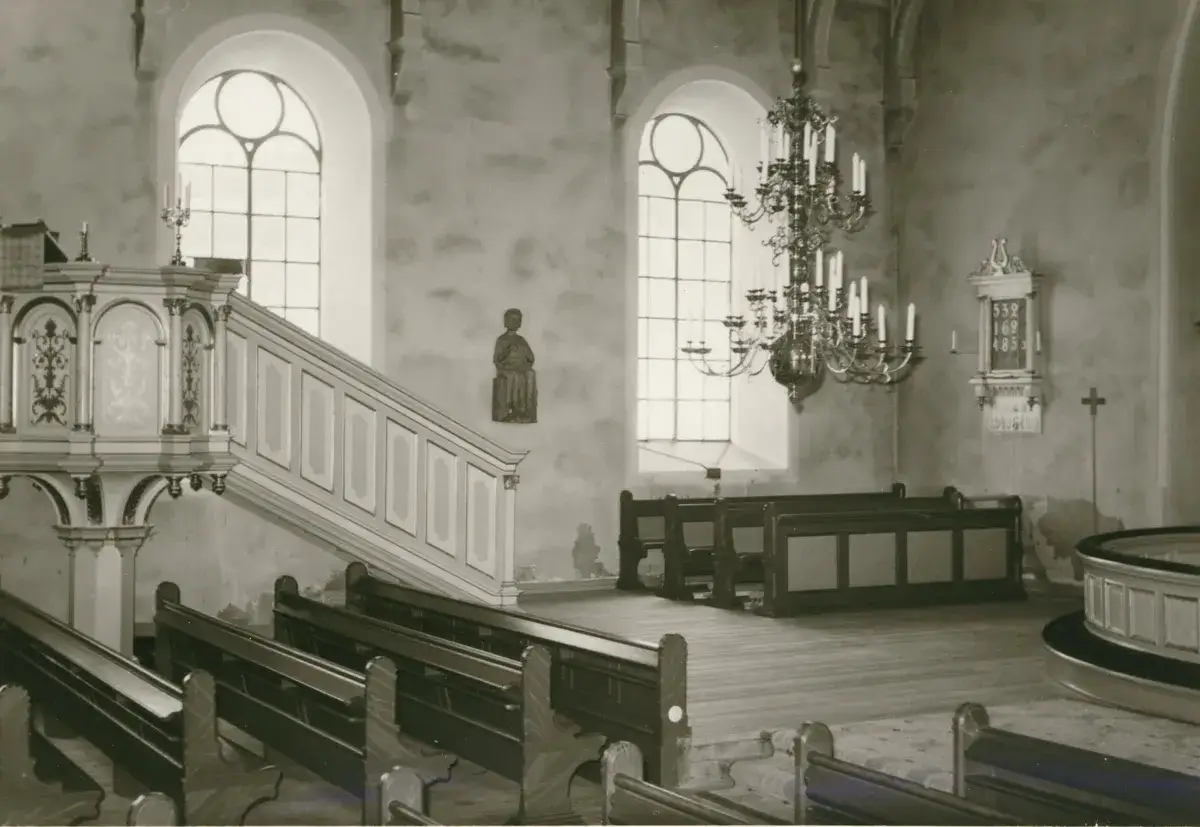 Kyrkans interi&ouml;r med predikstol, b&auml;nkar och en ljuskrona. Altare synonym &auml;r inte synligt, men kyrkan &auml;r en plats f&ouml;r andakt.