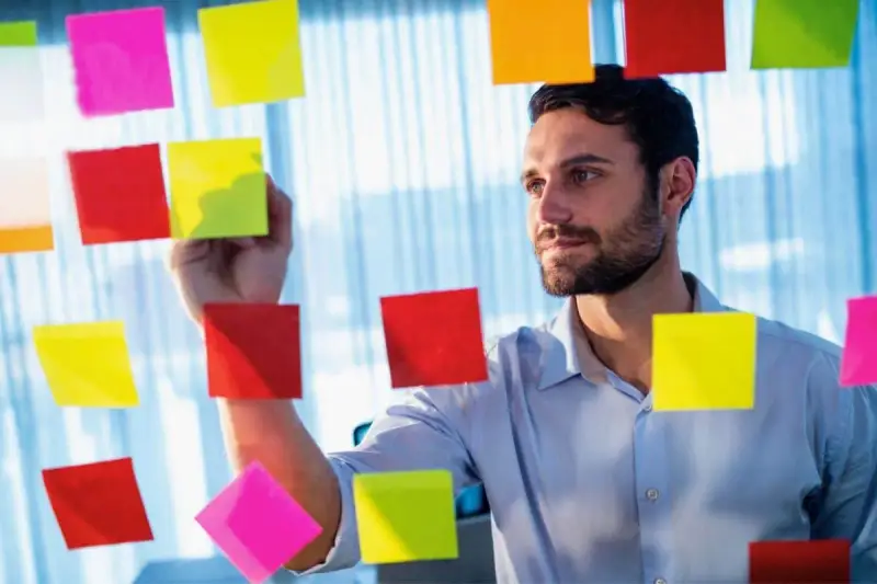 Man med skägg fäster post-it-lappar på en glasvägg, som en del av processen att skriva debattartikel.