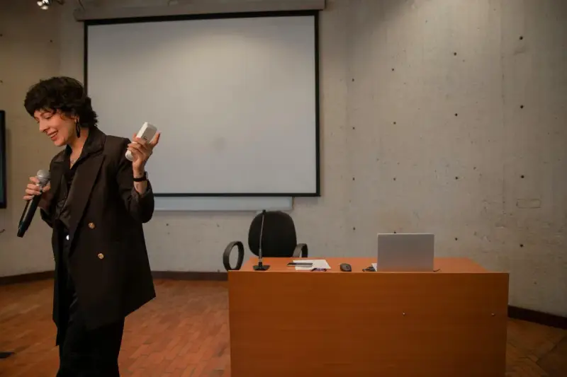 En kvinna håller mikrofon och en fjärrkontroll, redo att presentera en tes.